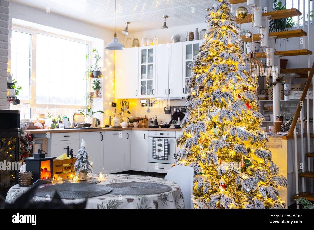 Decorazioni natalizie natalizie in cucina bianca, interni moderni del villaggio con un albero di Natale innevato e luci delle fate. Capodanno, atmosfera natalizia, casa accogliente, M Foto Stock