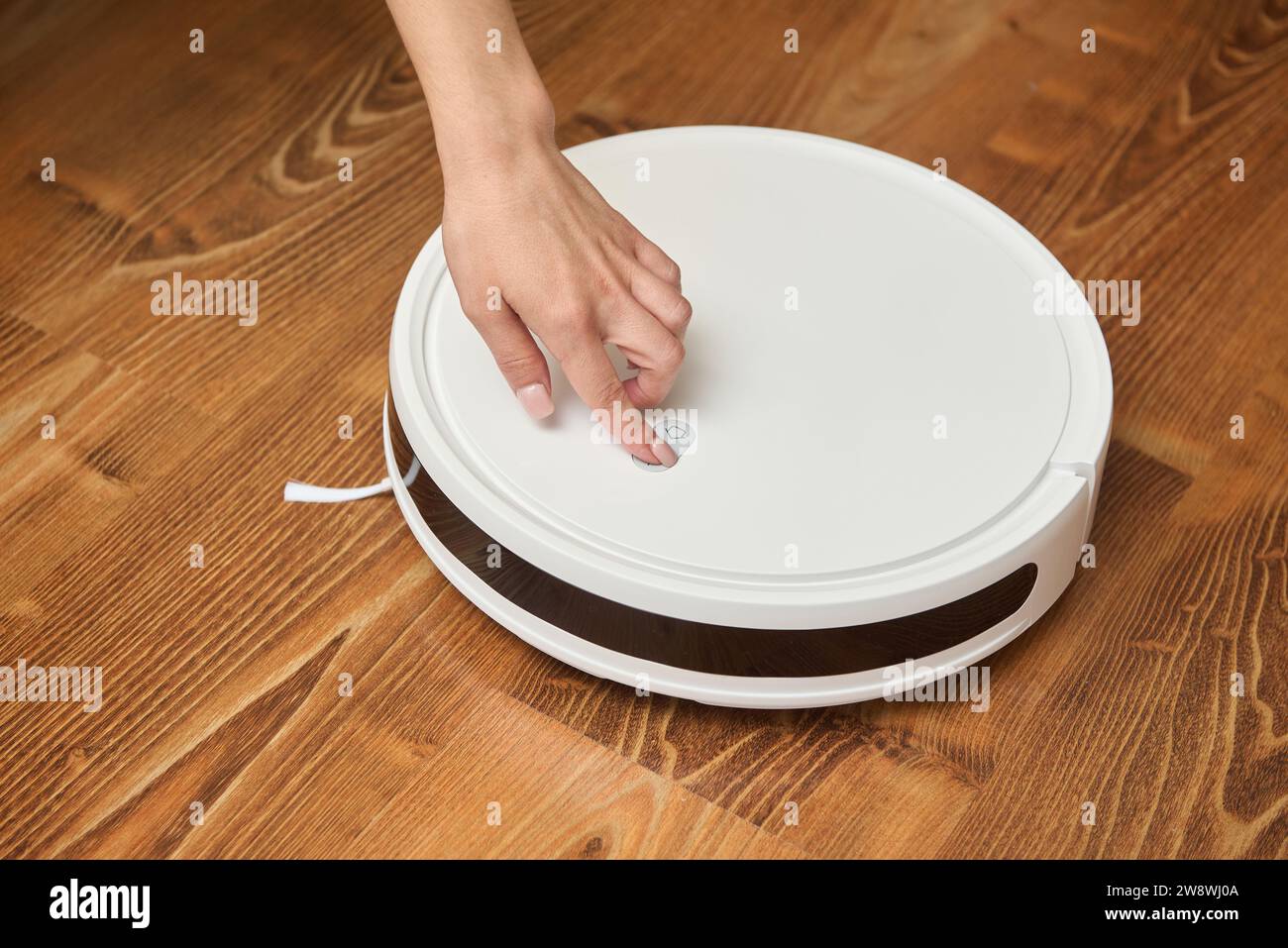 Una donna accende un aspirapolvere robot per pulirlo Foto Stock
