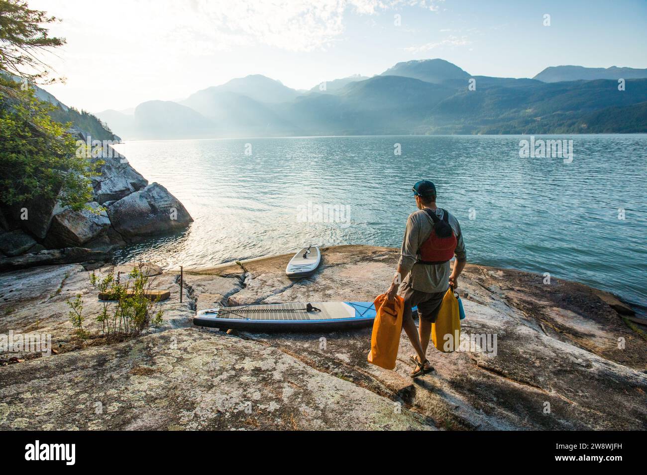 L'uomo trasporta sacchetti asciutti sul paddle board, preparandosi per il viaggio in pagaia Foto Stock