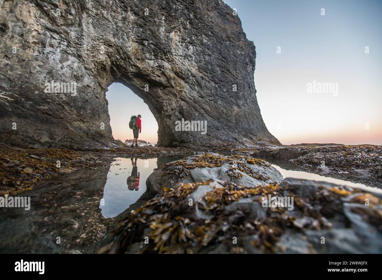 Angolo basso di backpacker in piedi a Hole-in-the-Wall, Rialto Beach Foto Stock