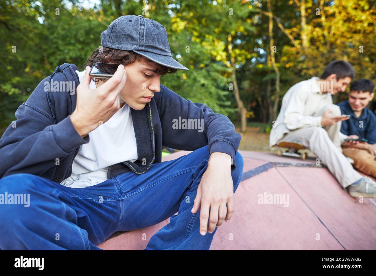 giovane che ascolta la voce attraverso l'altoparlante del telefono nello skate park Foto Stock