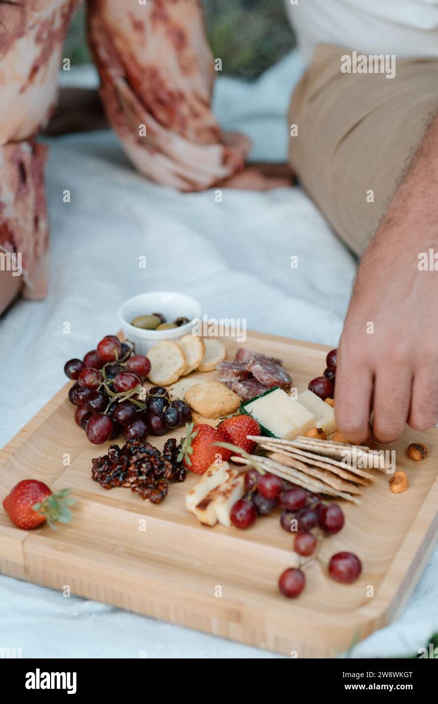Le mani afferrano la frutta dal tagliere di salumi durante la serata del giorno Foto Stock
