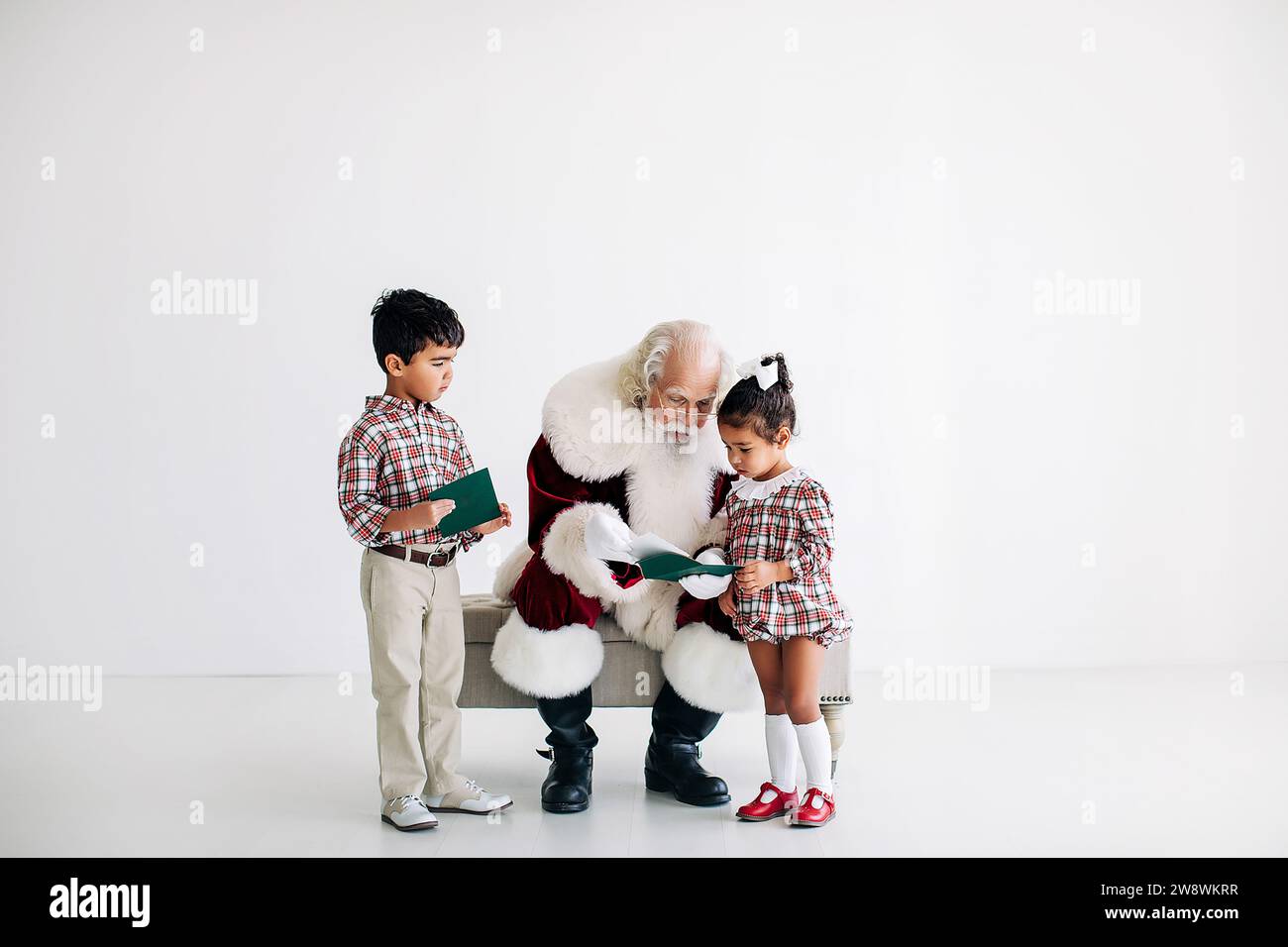 Fratelli che parlano con Babbo Natale con uno sfondo bianco pulito Foto Stock