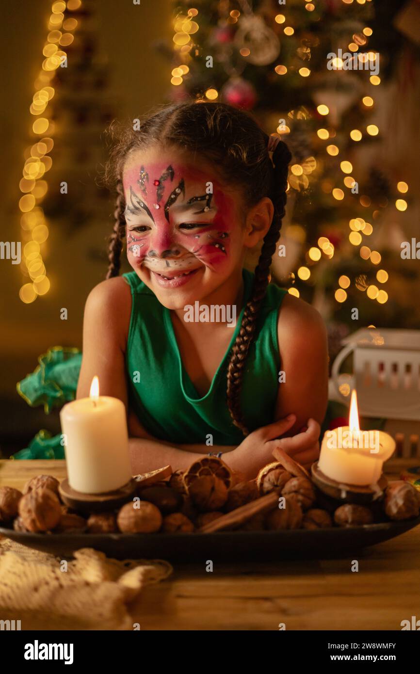 una piccola ragazza dalla pelle scura fa esplodere una candela, natale a casa, famiglia Foto Stock