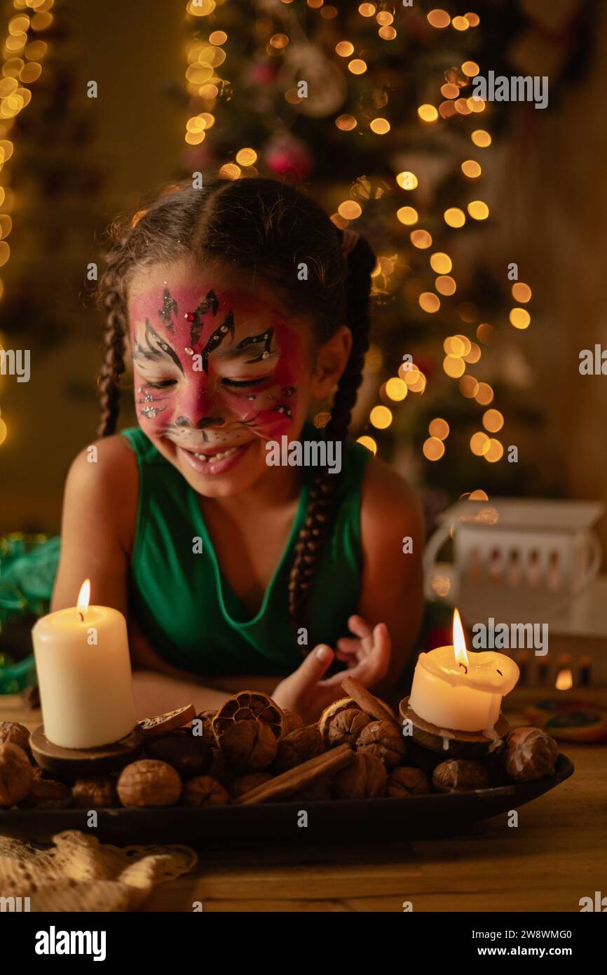 una piccola ragazza dalla pelle scura fa esplodere una candela, natale a casa, famiglia Foto Stock