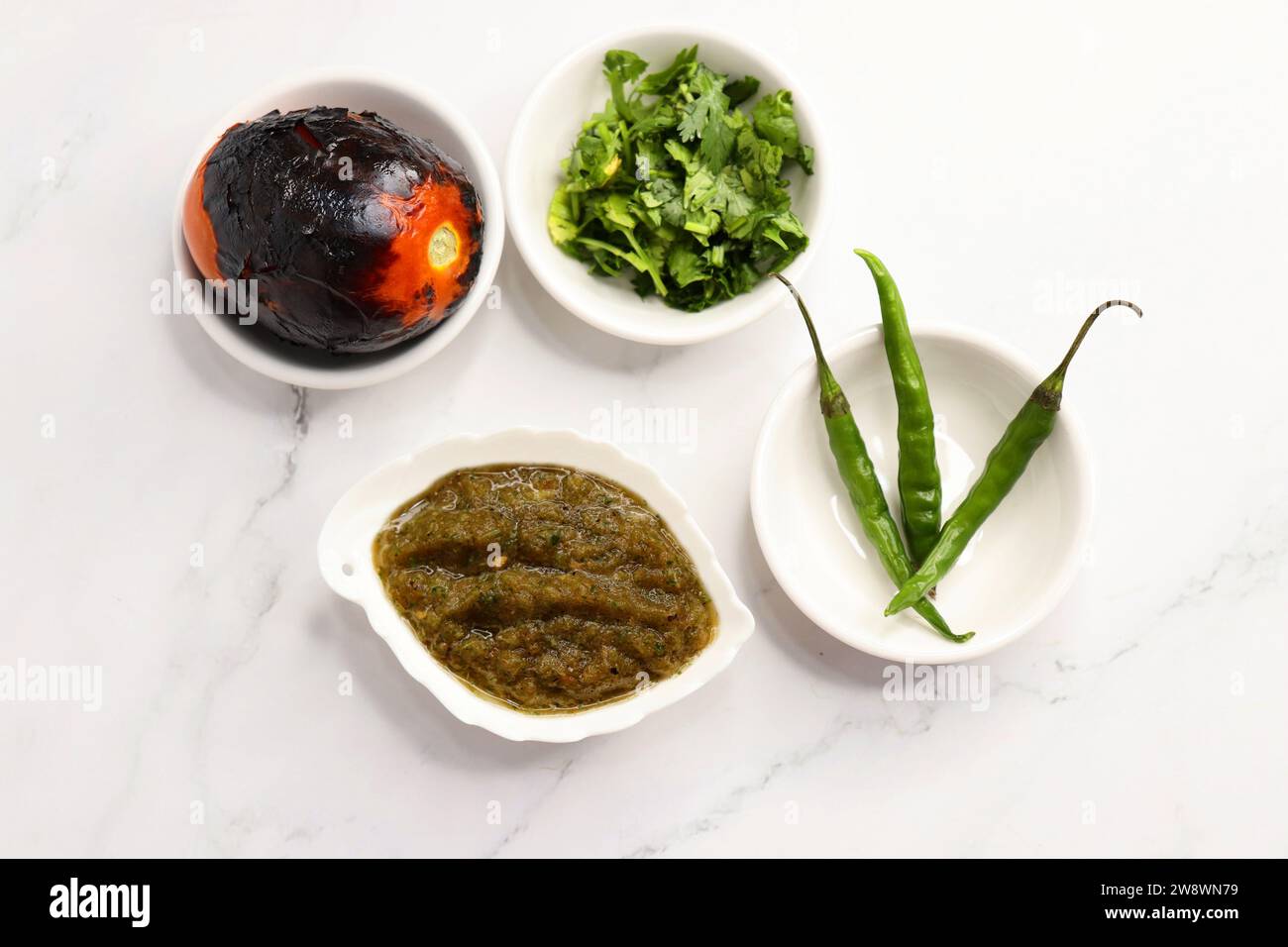 Salsa di pomodoro o chutney arrostiti fatti in casa serviti in un piccolo piatto di ceramica su sfondo bianco insieme agli ingredienti pomodoro arrosto e peperoncino verde. Foto Stock