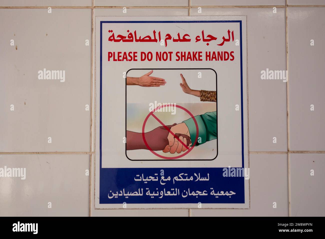 Cartello da parete nel mercato del pesce, in arabo e in inglese , (evitare di agitare la mano per prevenire la diffusione dell'infezione), Ajman, Emirati Arabi Uniti. Foto Stock