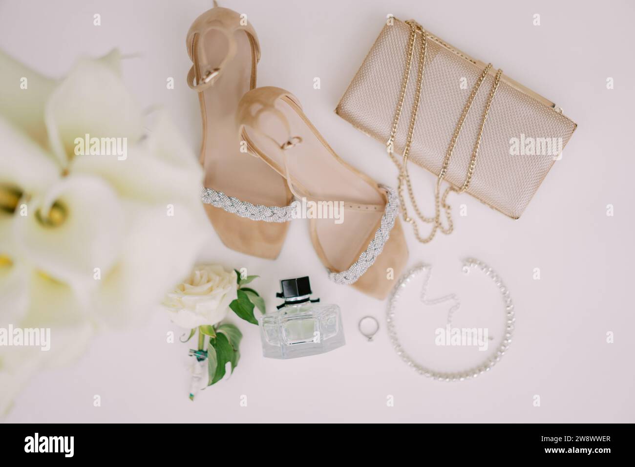 La fede nuziale si trova su un tavolo bianco vicino alle scarpe da sposa, alla borsa e al profumo. Vista dall'alto Foto Stock