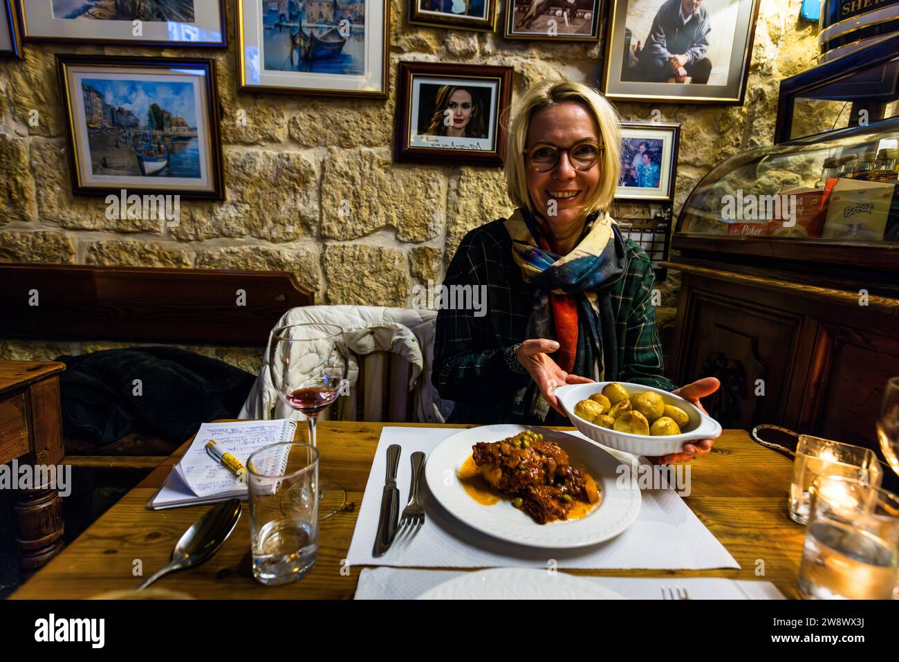 La giornalista Angela Berg tiene una ciotola di patate da accompagnare al piatto nazionale maltese fenek, uno stufato di coniglio, al ristorante Ta' Rosina a Sannat, Gozo, Malta. Una foto autografata di Angelina Jolie, che è stata ospite qui durante le riprese di "By the Sea" a Gozo nel 2014, è appesa al muro. Foto Stock