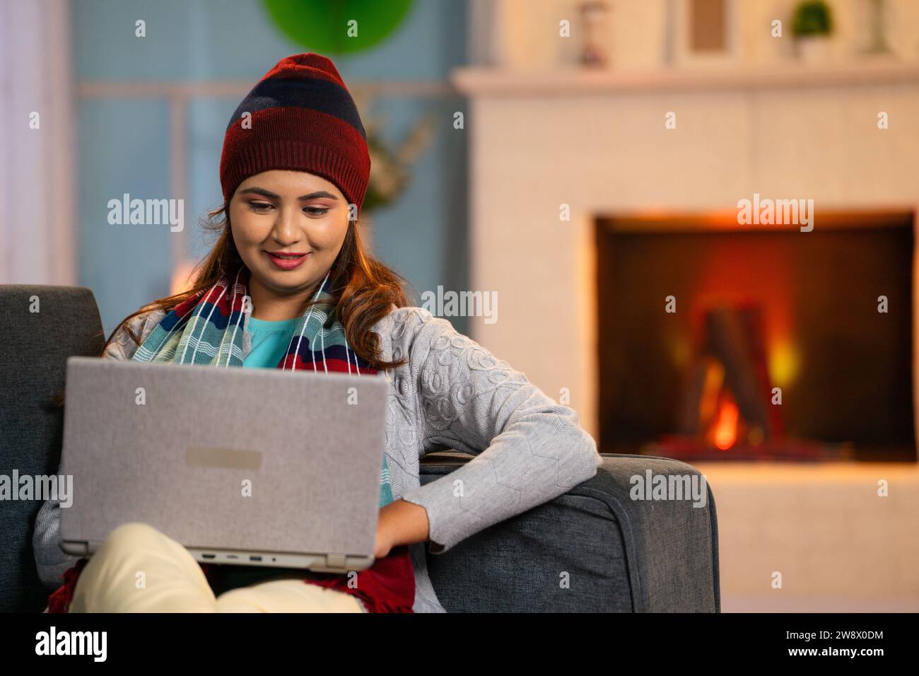 Felicemente calorosa donna con abbigliamento invernale che utilizza o lavora su un computer portatile a casa sul divano - concetto di freelance, lavoro e libertà Foto Stock