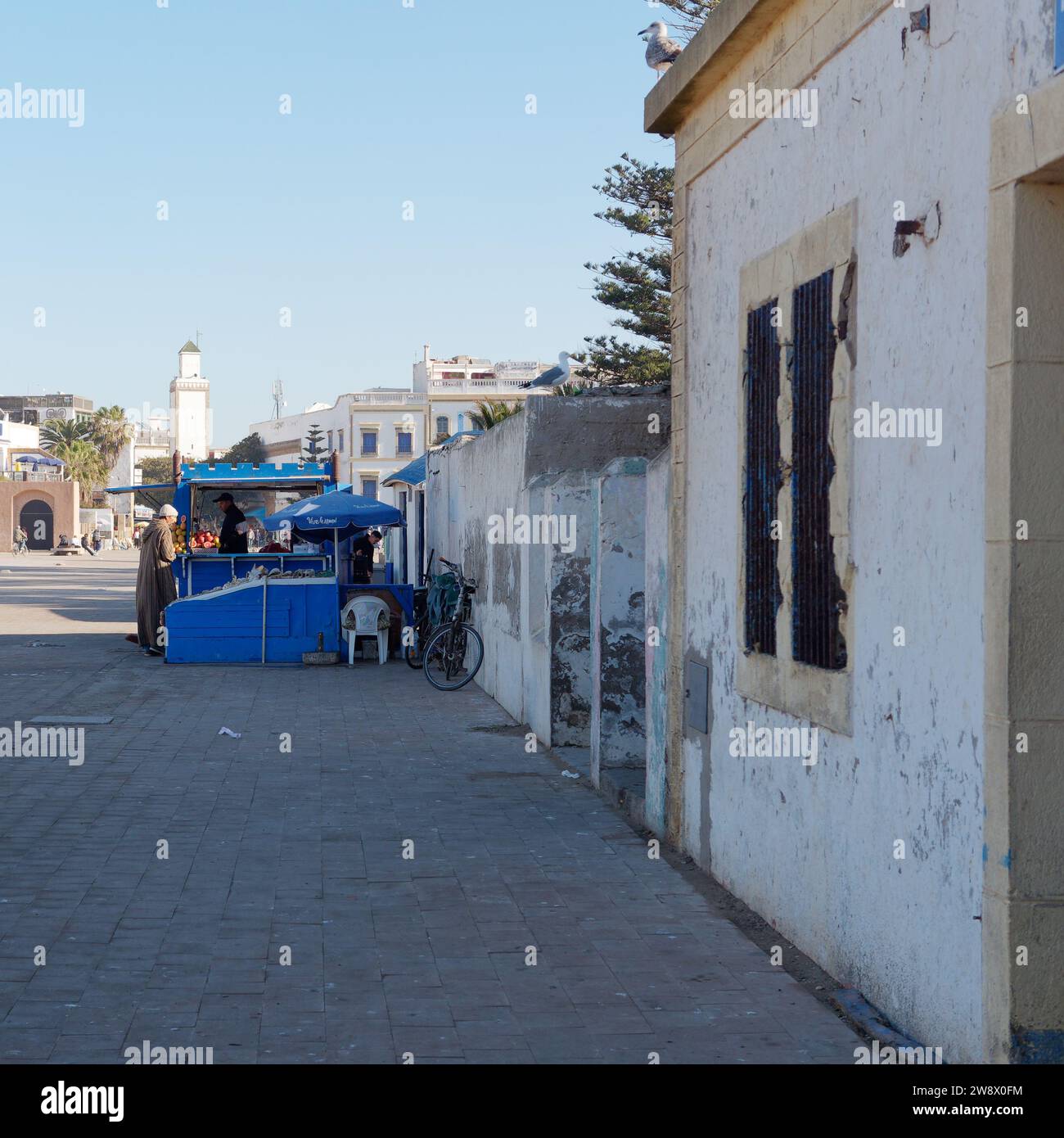 Strada con la banchina del mercato blu e la torre nella medina alle spalle. Essaouira, Marocco. 22 dicembre 2023 Foto Stock