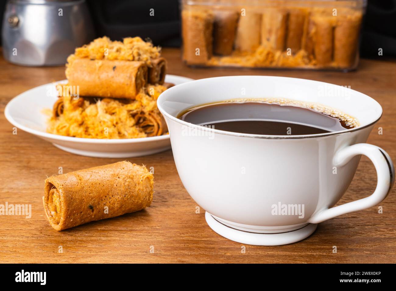 Tazza di caffè nero caldo con una pila di panini di maiale croccanti e croccanti e macchina per il caffè in moka su un tavolo di legno. Foto Stock