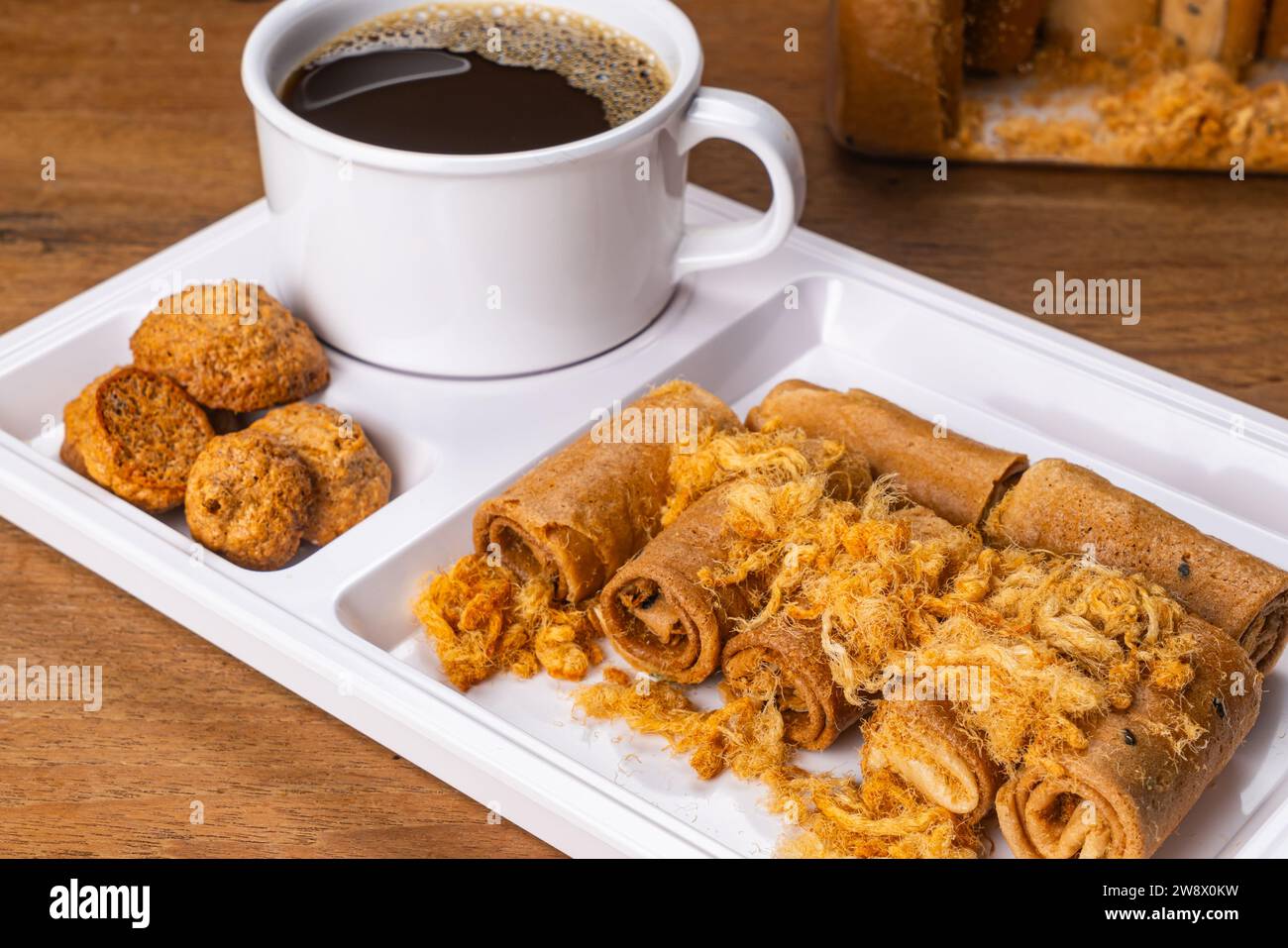 Alta pila di meringa croccante al cocco e croccante rotolo di cocco con maiale secco e una tazza di caffè nero in vassoio di plastica su Wo Foto Stock
