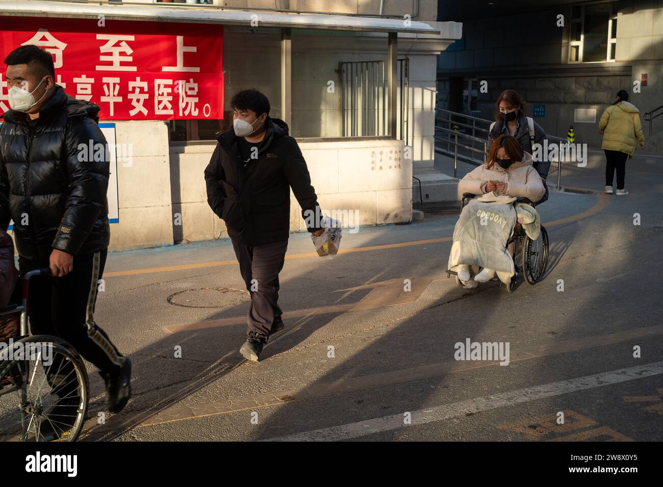 Una ragazza spinge il suo compagno malato su una sedia a rotelle in un ospedale a Pechino, in Cina. 22 dicembre 2023 Foto Stock