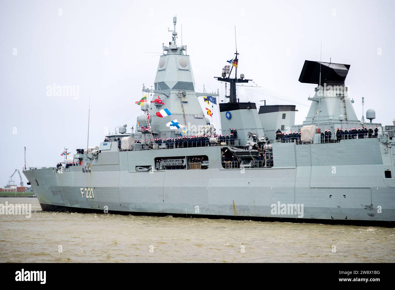 Wilhelmshaven, Germania. 22 dicembre 2023. I membri dell'equipaggio che indossano cappelli di Natale si trovano a bordo della fregata "Hessen" mentre la nave entra nel porto presso la base navale. Con circa 230 militari e donne a bordo, la fregata tornò al suo porto di origine poco prima di Natale. Negli ultimi cinque mesi, la nave aveva preso parte a tre grandi manovre e a molte esercitazioni nel Mare del Nord, nel Mar Baltico e nell'Atlantico settentrionale. Credito: Hauke-Christian Dittrich/dpa/Alamy Live News Foto Stock