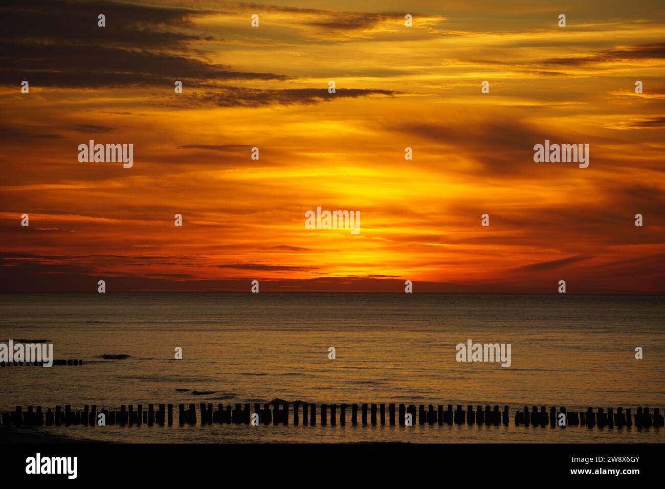 La foto raffigura un tramonto sul Mar Baltico, con il cielo dipinto in sfumature di arancione e adornato da nuvole sparse. Tramonto in Germania. Foto Stock