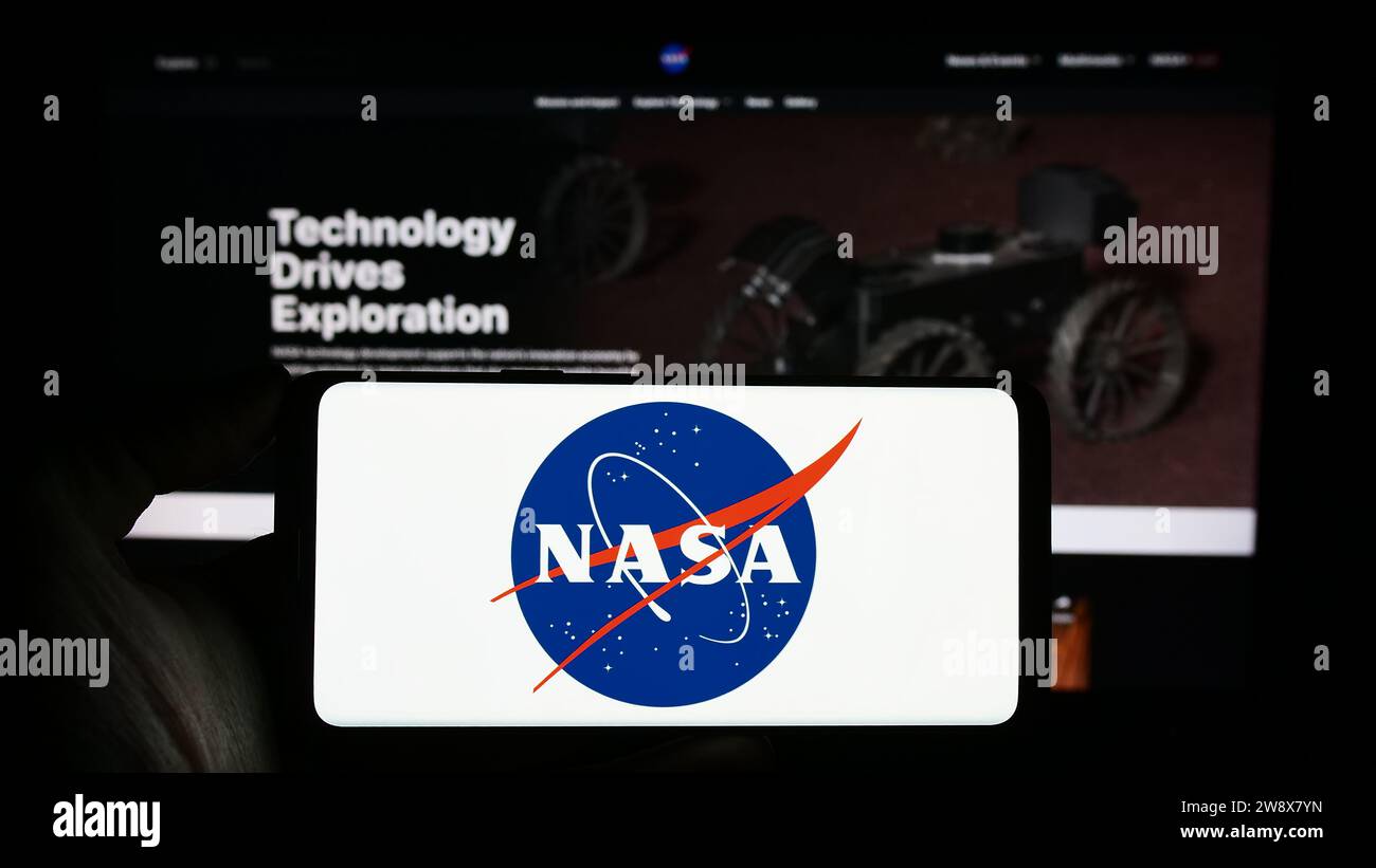 Persona che possiede uno smartphone con il logo della NASA (National Aeronautics and Space Administration) davanti al sito Web. Concentrarsi sul display del telefono. Foto Stock