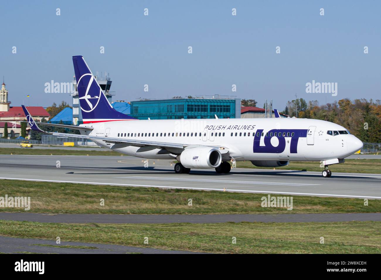 LOT Polish Airlines Boeing 737-800 decolla dall'aeroporto di Leopoli, con torre ATC sullo sfondo Foto Stock