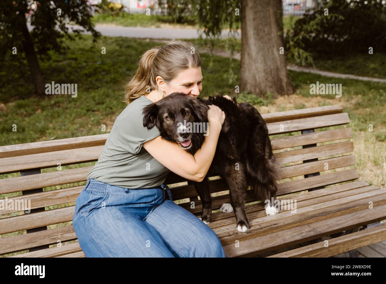 Donna matura che abbraccia il cane sulla panchina nel parco Foto Stock