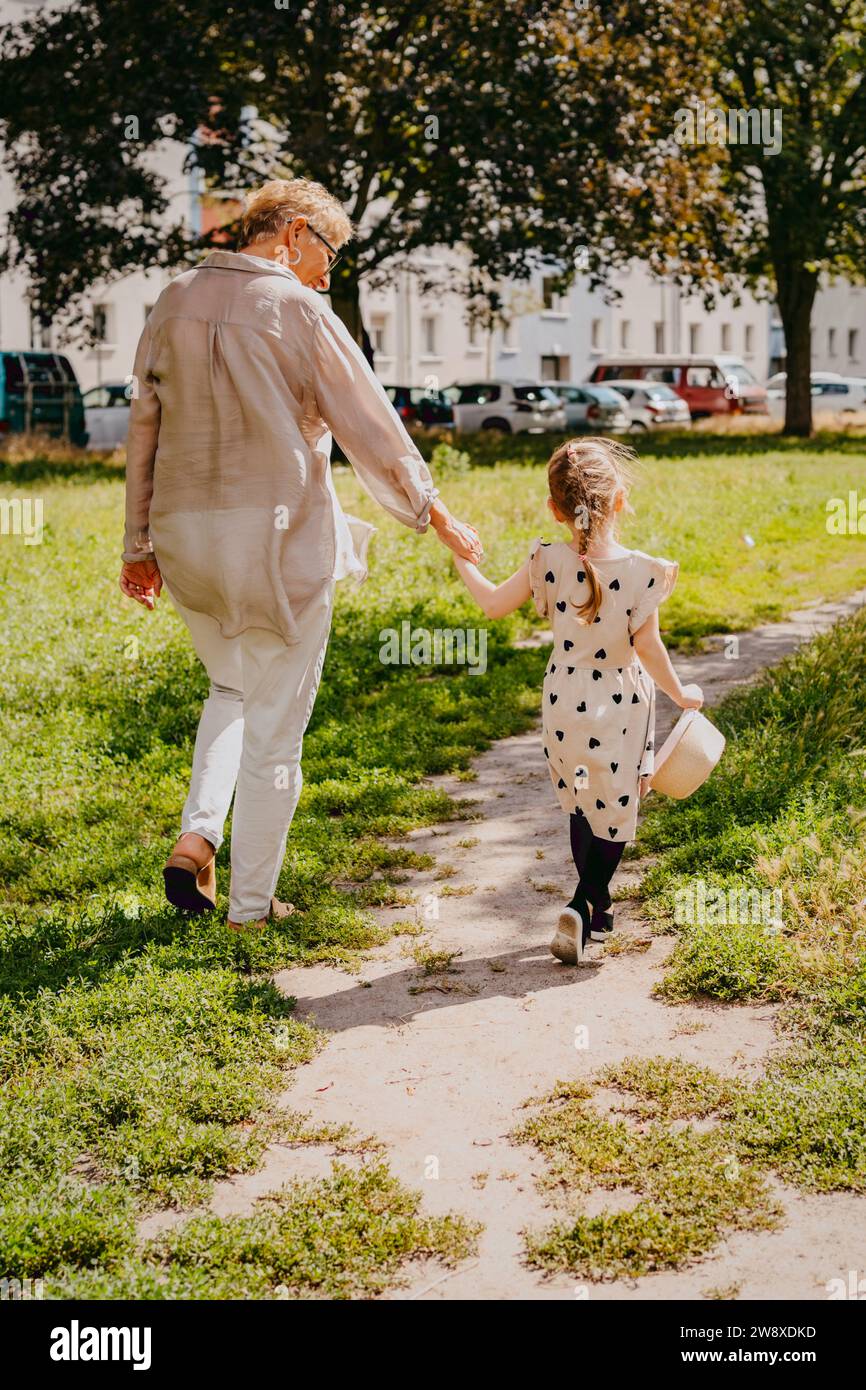 Donna anziana che tiene per mano la nipote che cammina al parco Foto Stock