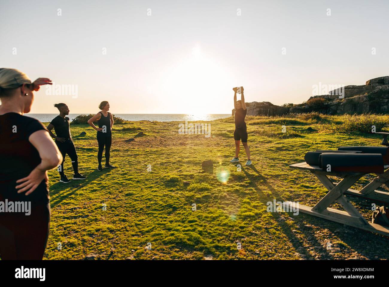 Istruttore femminile che assiste il team durante l'allenamento di gruppo contro il cielo in spiaggia Foto Stock