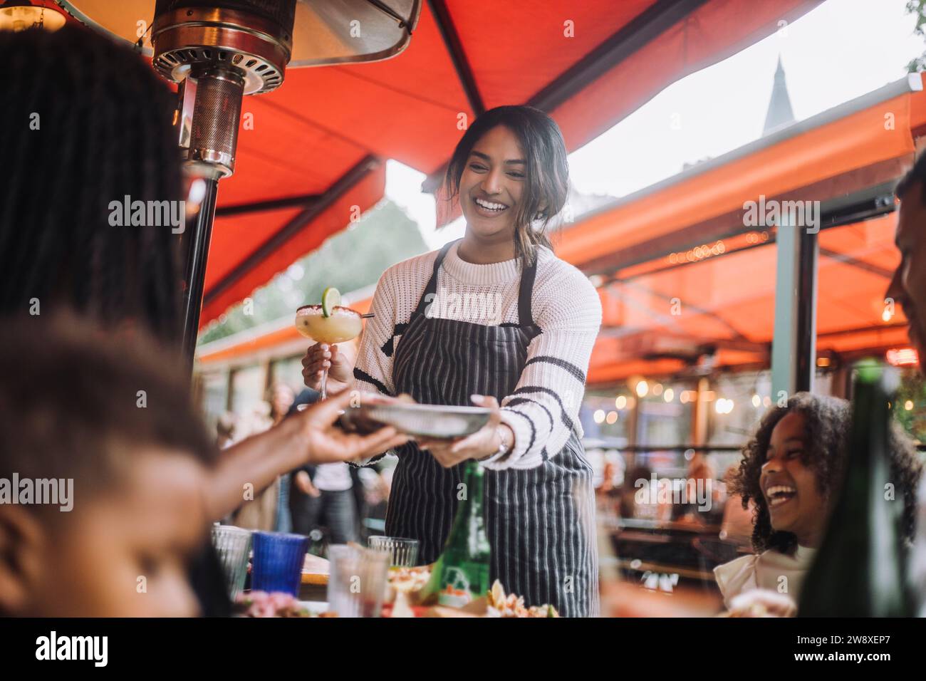 Cameriera sorridente che serve cibo e bevande ai clienti che si divertono al ristorante Foto Stock