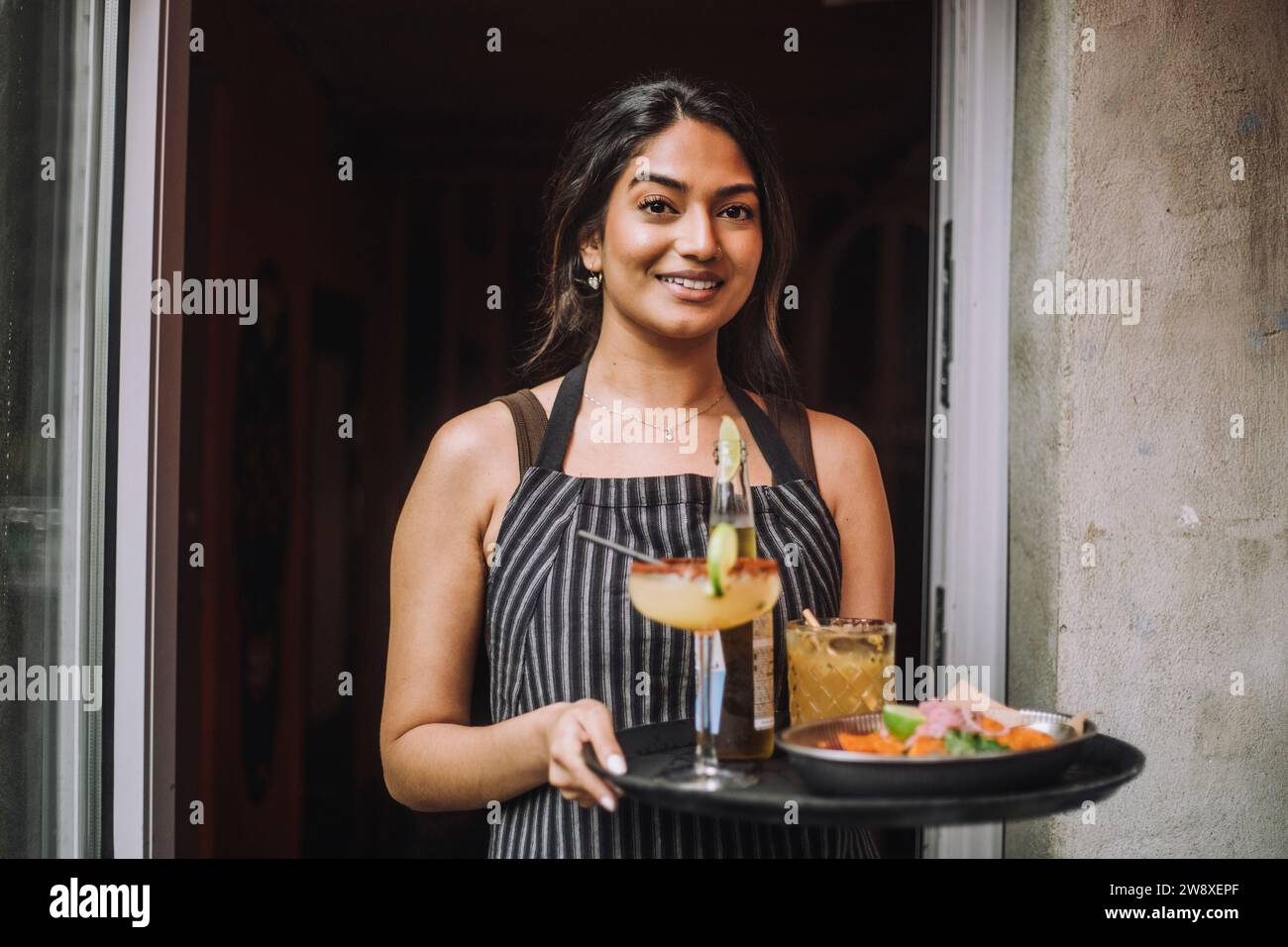 Ritratto di una cameriera sorridente che tiene un vassoio di cibo e bevande all'ingresso del bar Foto Stock