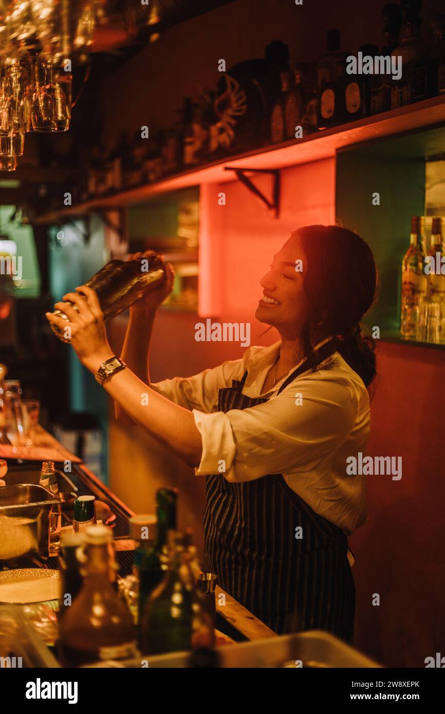 Sorridente barista che prepara il cocktail mentre lavora al bancone del bar Foto Stock