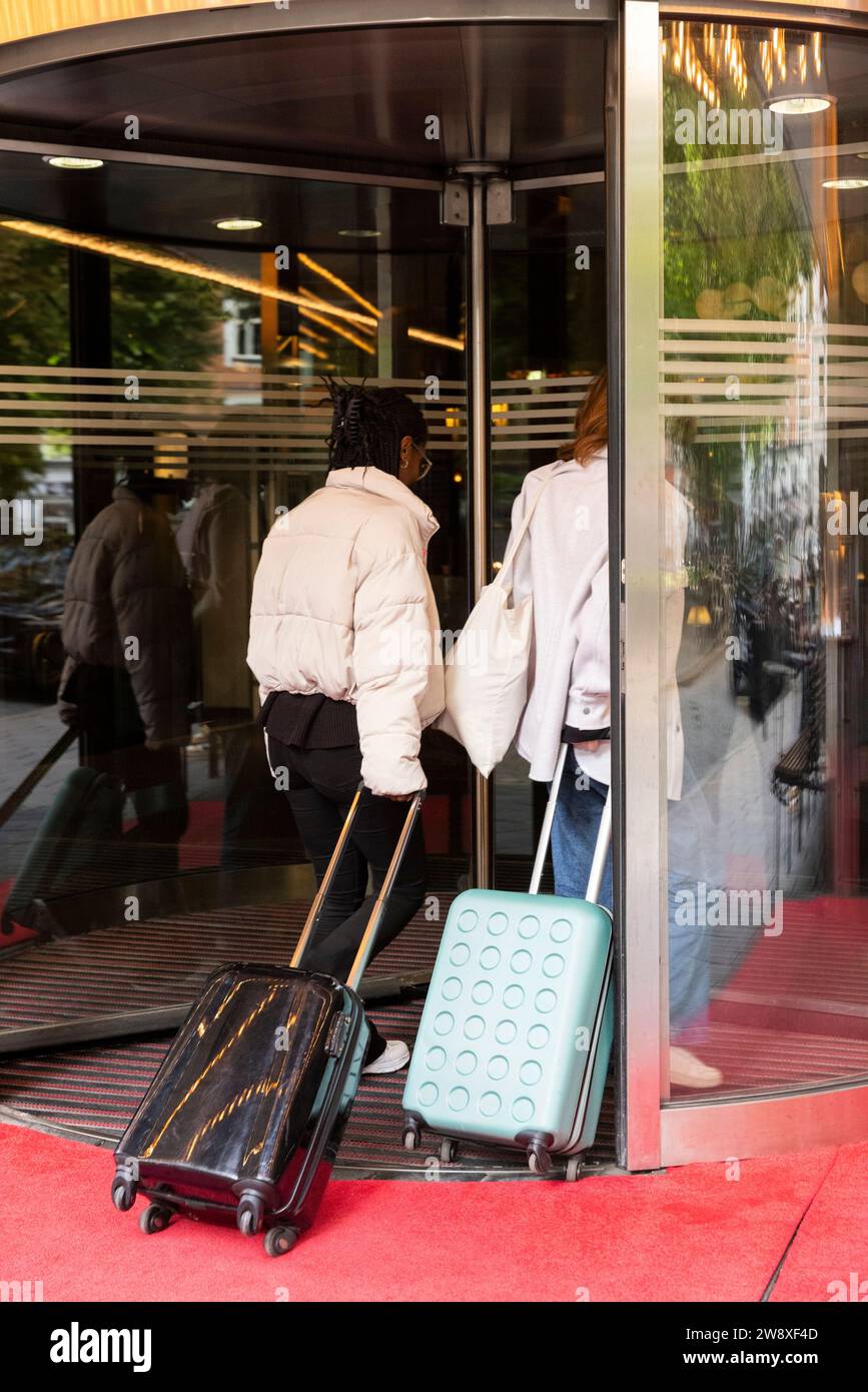 Giovani turisti donne con bagagli su ruote che entrano attraverso la porta girevole dell'hotel Foto Stock