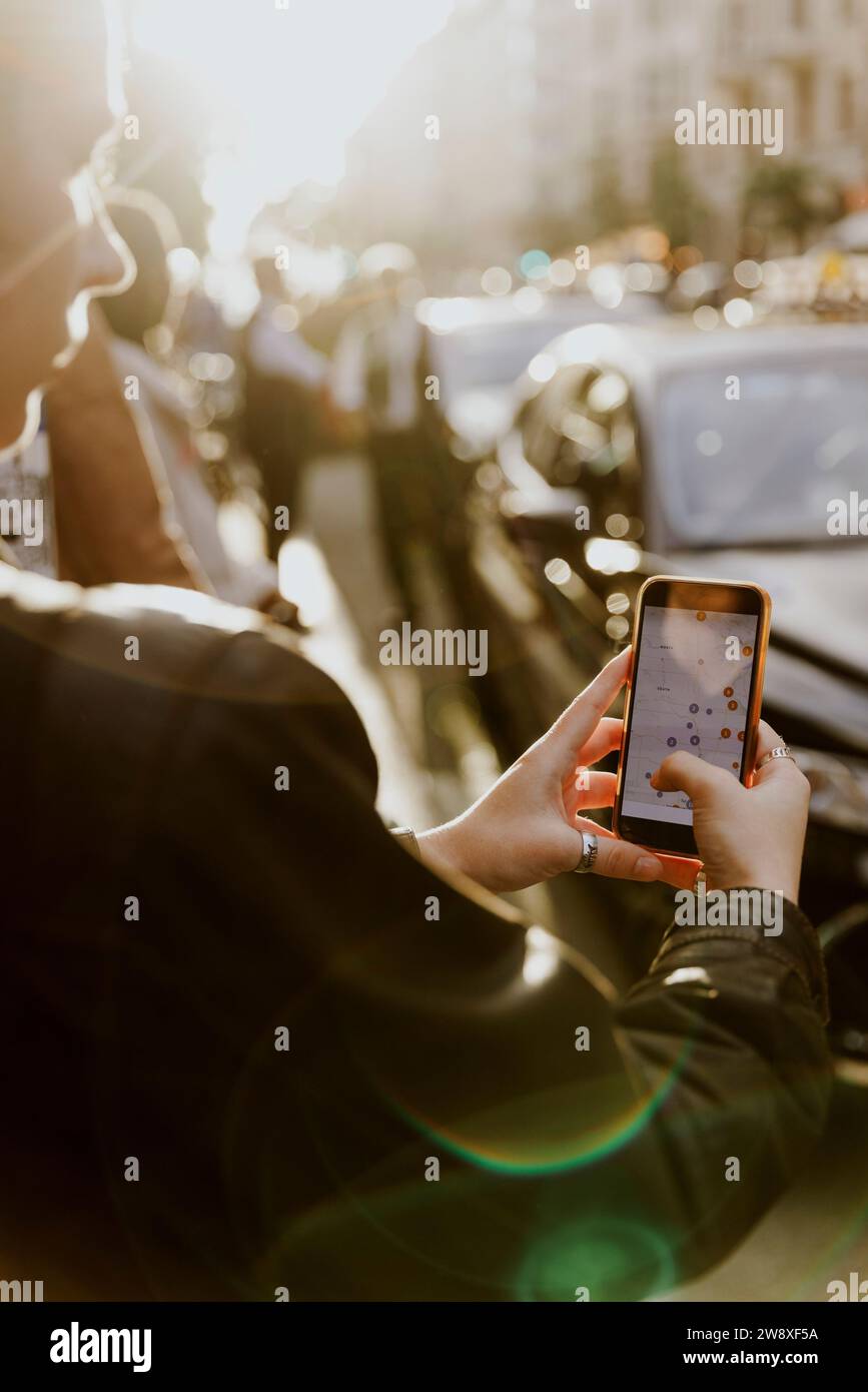 Turista femminile che accede al GPS tramite smartphone nelle giornate di sole in città Foto Stock