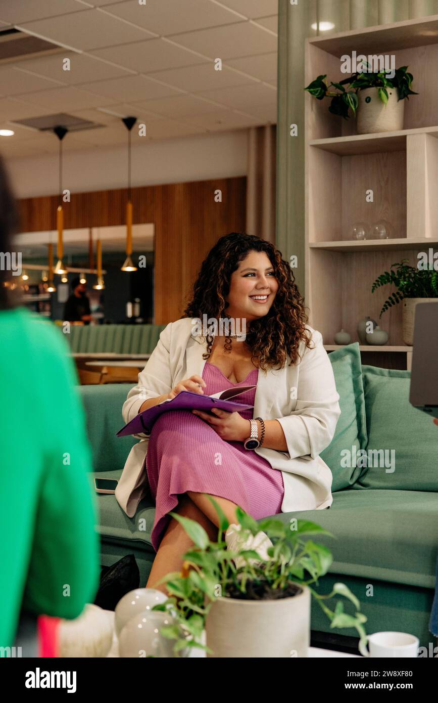 Una donna sorridente professionista d'affari seduta con file sul divano in ufficio Foto Stock