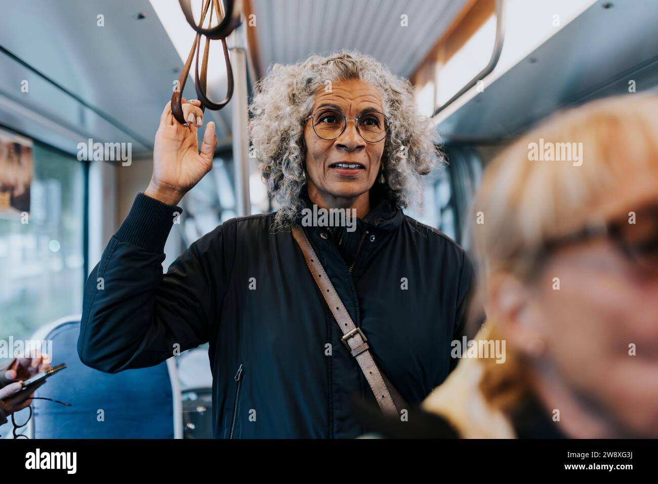 Donna anziana in piedi in autobus mentre viaggia per lavoro Foto Stock