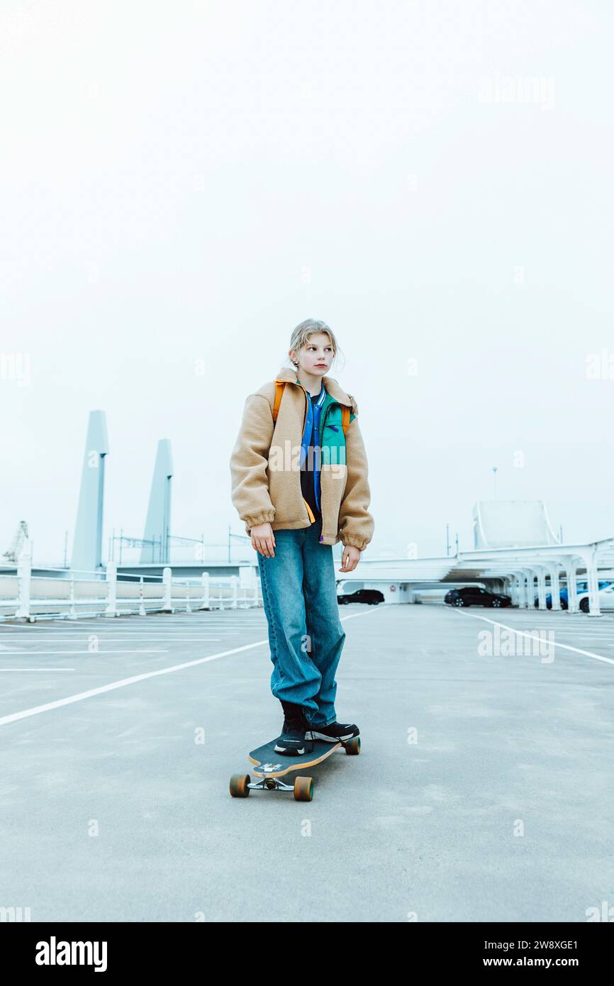 Ragazza che fa skateboard in strada contro il cielo limpido durante il fine settimana Foto Stock