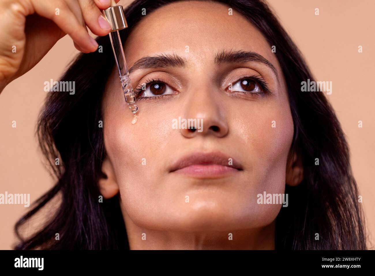 Primo piano di una donna affascinante che tiene una pipetta con siero rigenerante con acido ialuronico. Ragazza attraente con bella pelle sana e idratante Foto Stock