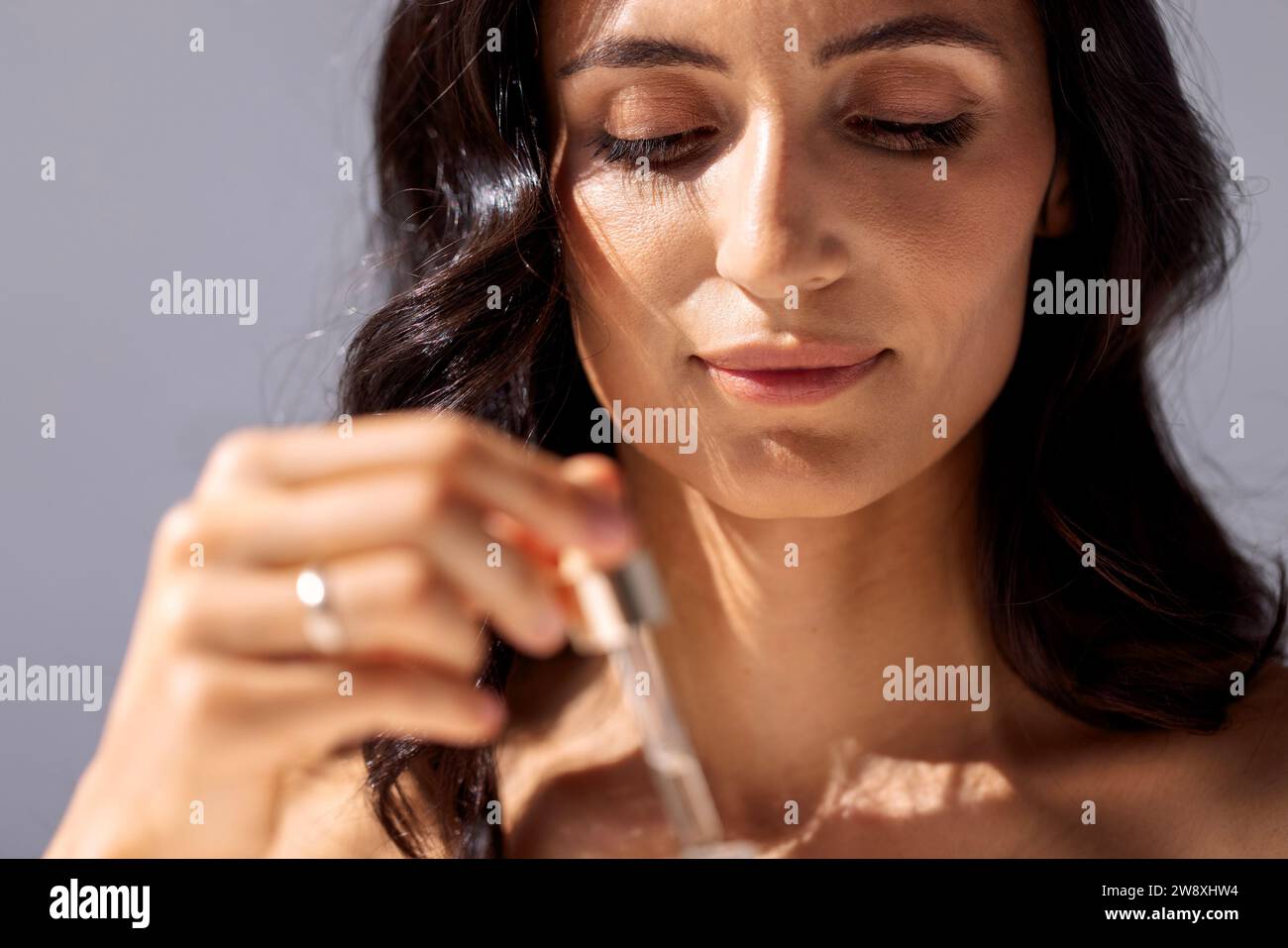 Donna affascinante con pelle e capelli perfettamente sani pipetta con siero rigenerante con acido ialuronico. Ragazza attraente con anti idratante Foto Stock