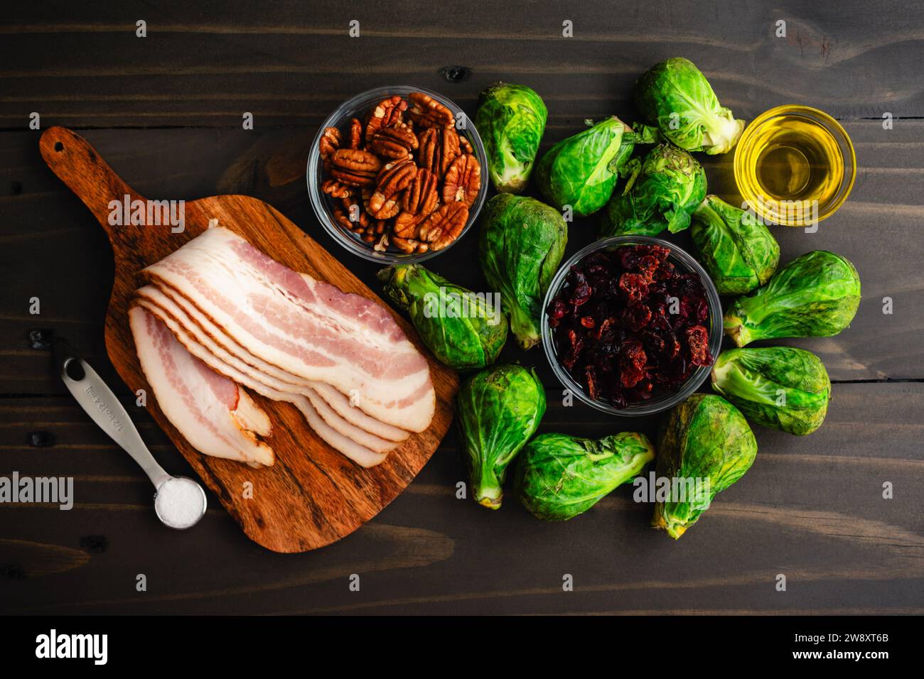 Cavoletti di Bruxelles con pancetta, noci pecan e mirtilli rossi ingredienti: Cavoletti di Bruxelles crudi, strisce di pancetta e altri ingredienti su un tavolo di legno Foto Stock