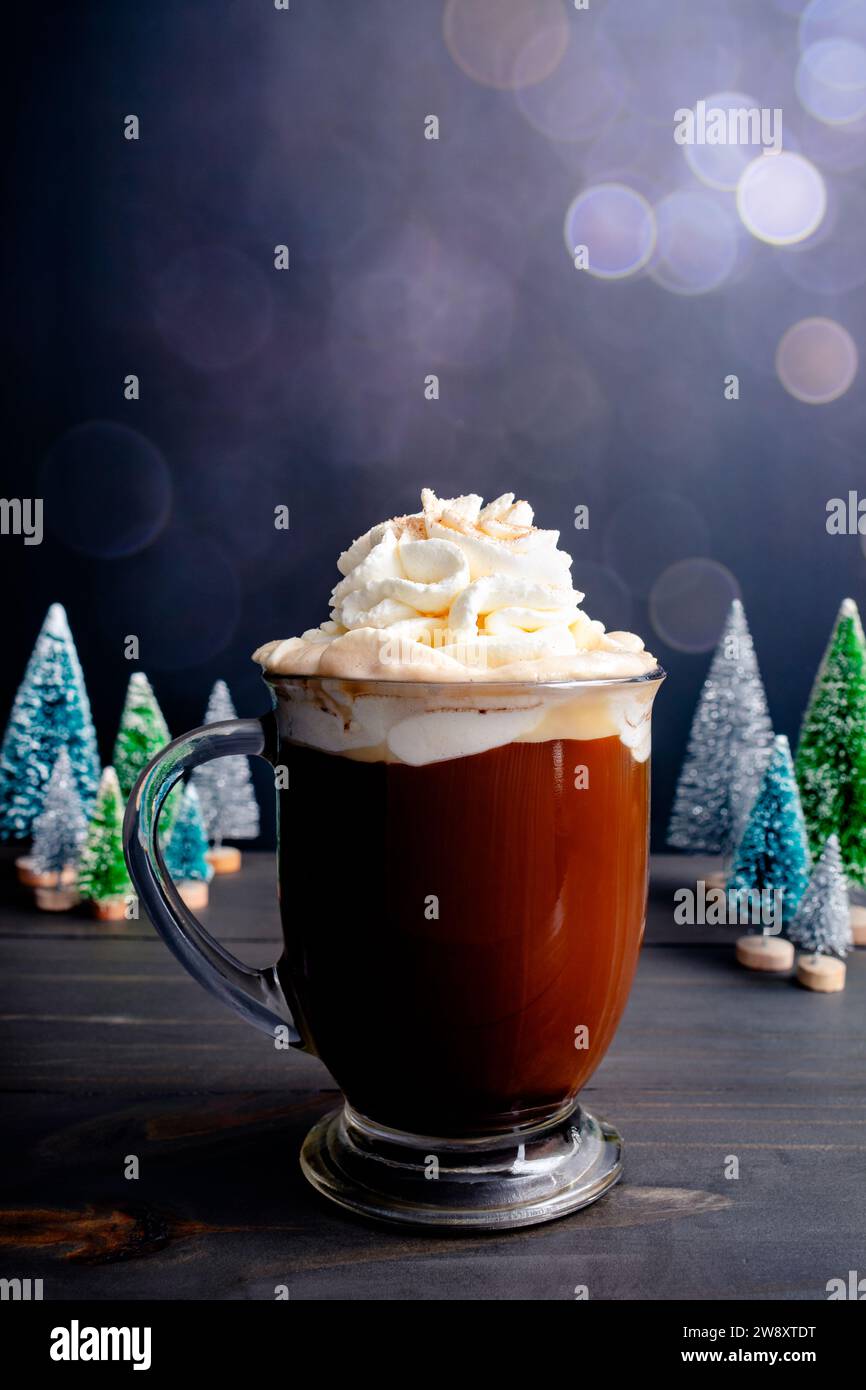 Caffè di Natale speziato condito con panna montata e zucchero alla cannella: Grande tazza in vetro di caffè speziato appena fatto con alberi di Natale in miniatura Foto Stock