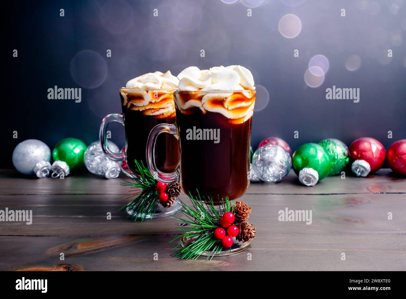 Caffè di Natale speziato con panna montata: Due tazze in vetro di caffè speziato appena fatto con ornamenti natalizi sullo sfondo Foto Stock