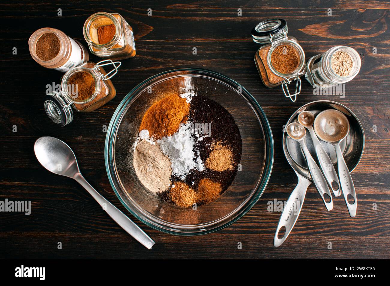 Preparazione della miscela di caffè natalizio piccante fatta in casa: Caffè macinato con zucchero in polvere, cannella, cardamomo e altre spezie macinate in un recipiente di miscelazione in vetro Foto Stock