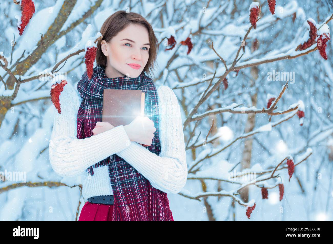 Ritratto di una ragazza affascinante che abbraccia un libro nella foresta invernale. Concetto di Natale, feste invernali, passeggiate nei boschi, vacanze. Misto Foto Stock