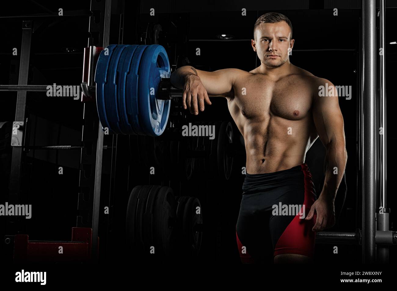 Il sollevatore di pesi appoggia la mano sul campanile e guarda in avanti minacciosamente. Vista frontale Foto Stock