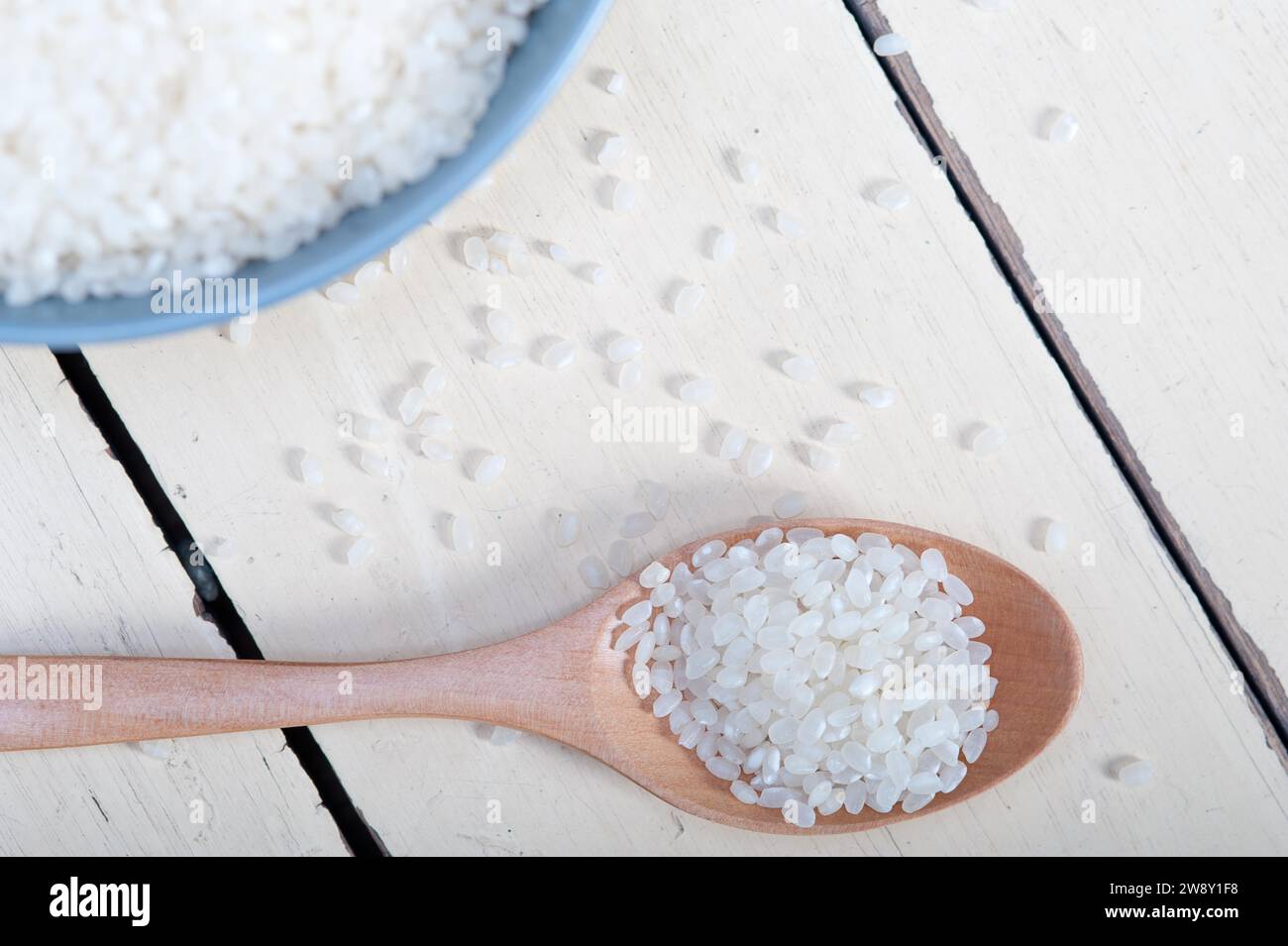 Riso bianco crudo su cucchiaio di legno e ciotola blu per primi piani estremi, fotografia alimentare Foto Stock