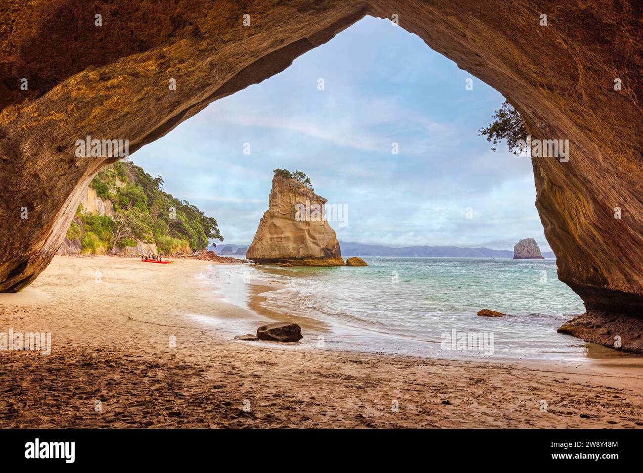 Vista da una grotta che si apre su una spiaggia sabbiosa e un solitario affioramento roccioso nel mare, Cathedral Grove, Coromandel, nuova Zelanda Foto Stock
