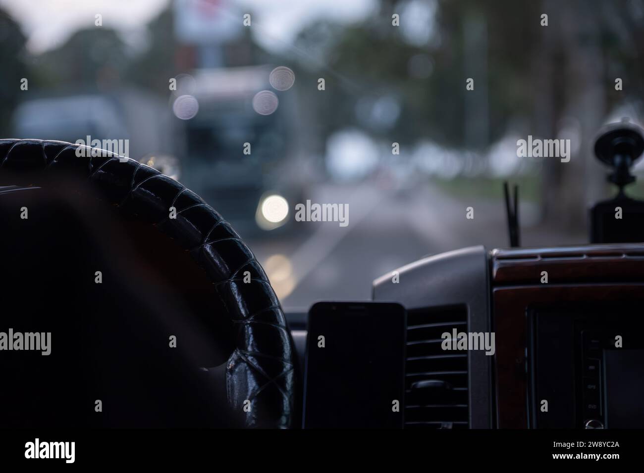 le mani di un vecchio mentre si guida su strada con luci sfocate e traffico automobilistico Foto Stock
