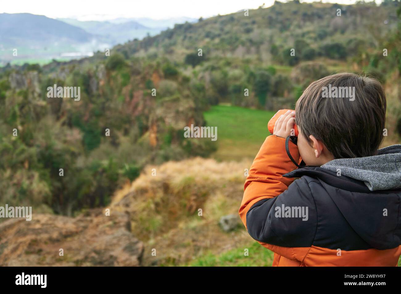 Bambino elementare che esplora le montagne con un binocolo. Foto Stock