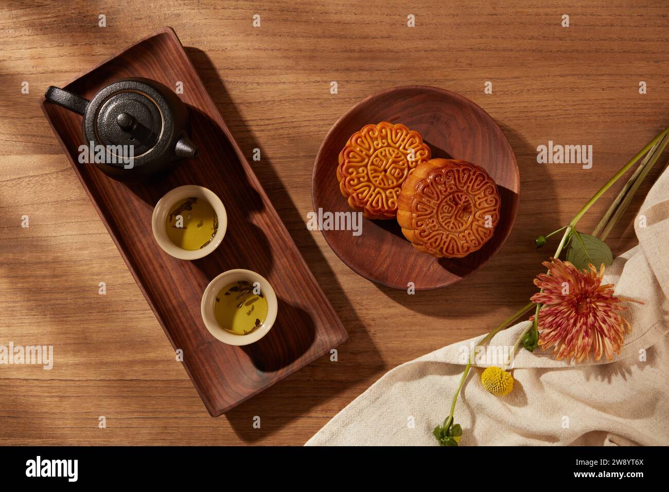 Sfondo del tradizionale festival cinese di metà autunno con torte lunari, set di tè su vassoi di legno e bellissimo fiore su tessuto bianco. Foto in stile cinese Foto Stock