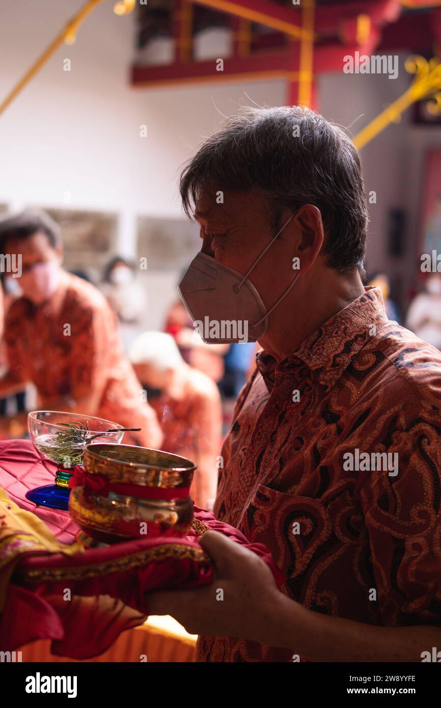 Bandung, Indonesia - 8 gennaio 2022: Il vecchio porta le offerte all'altare mentre prega con i monaci all'interno del tempio del Buddha Foto Stock