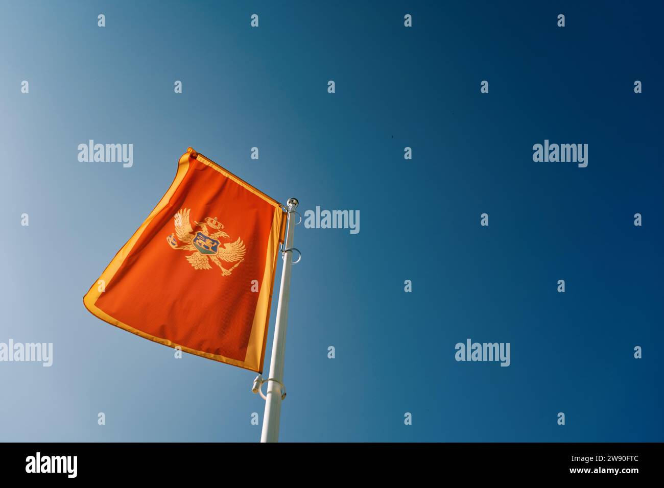 La bandiera del Montenegro fluttua su un'asta bianca contro un cielo blu Foto Stock