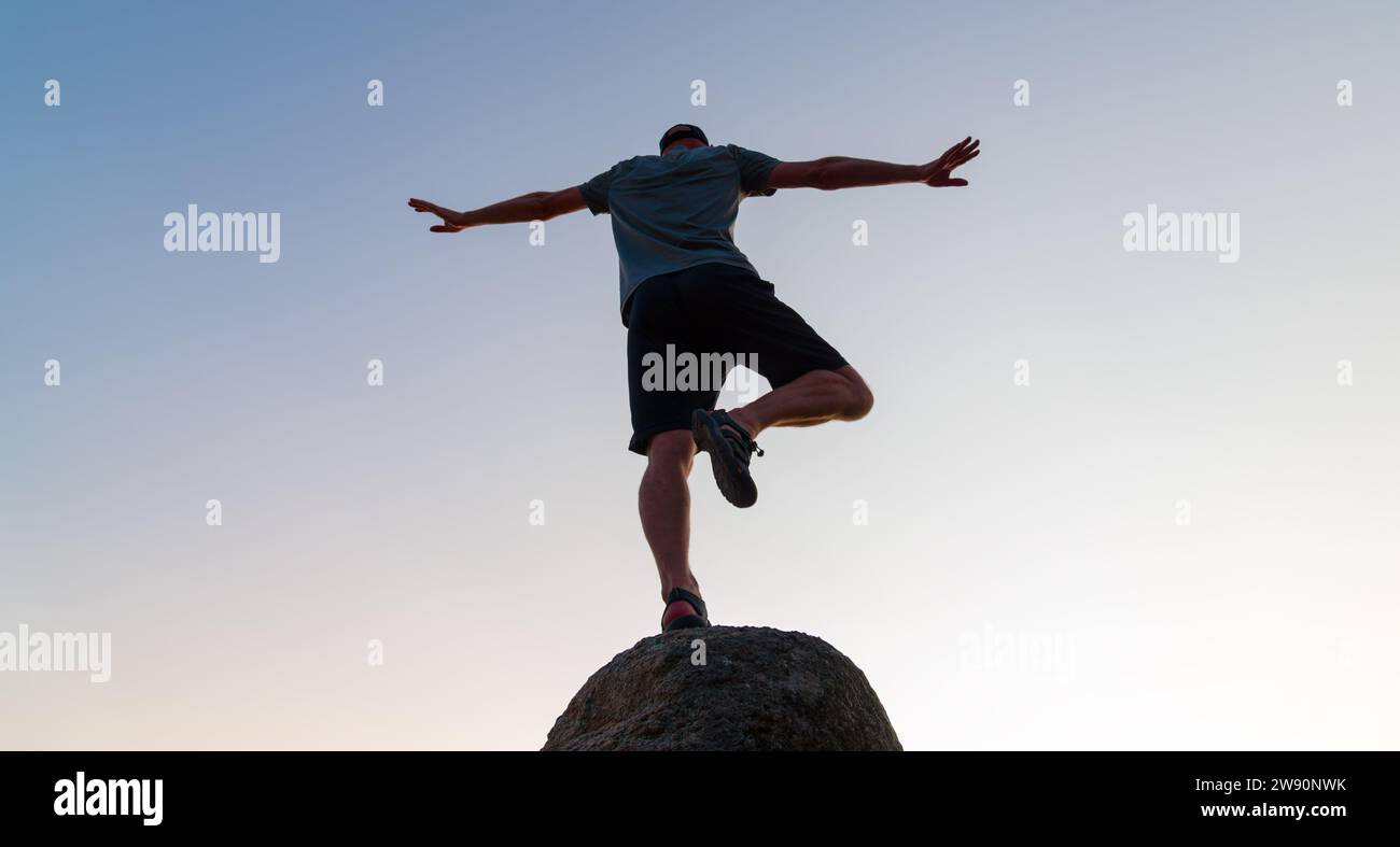 silhouette di un uomo che pratica yoga su una roccia all'aperto al tramonto, concetto di equilibrio e calma mente e corpo Foto Stock
