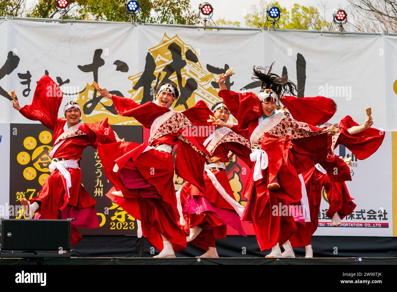 Squadra di ballerini giapponesi yosakoi sul palco che balla con gonne rosse e tuniche yukata a maniche lunghe tenendo naruko e clappers. Kyusyu Gassai festival. Foto Stock